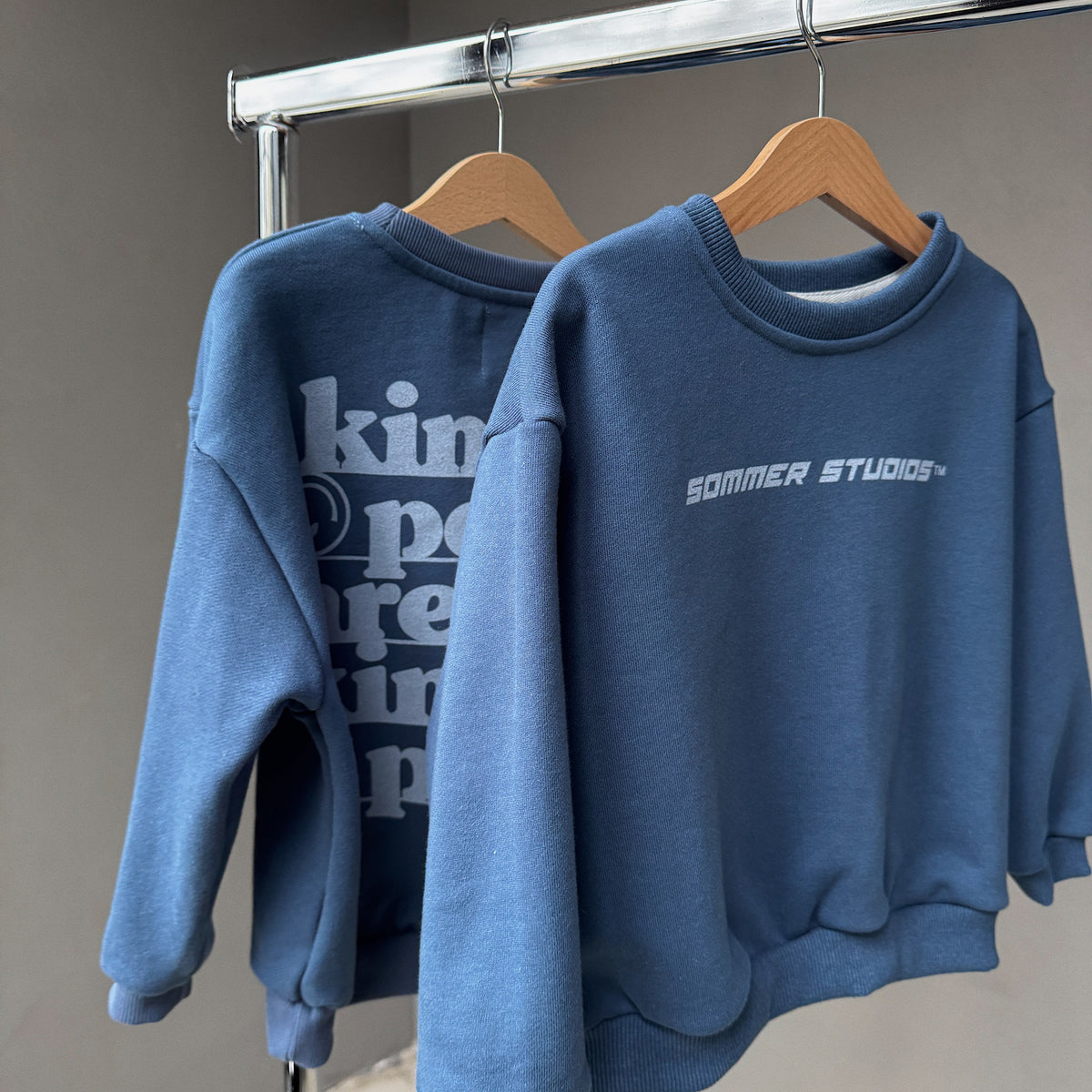 Two blue sweatshirts hanging on a rack with visible branding.